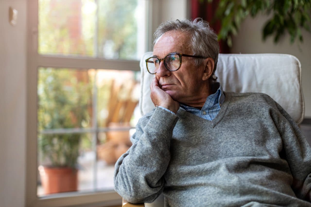 Older man looking out window of home.