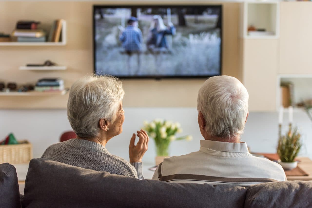 Older husband and wife sitting on the couch watching TV.