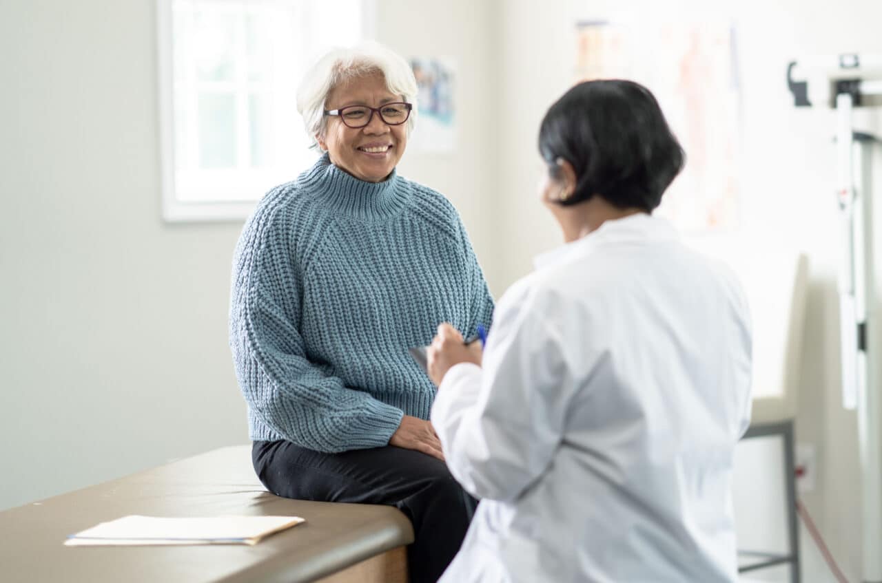 Older woman sitting on an exam table and talking with her doctor.