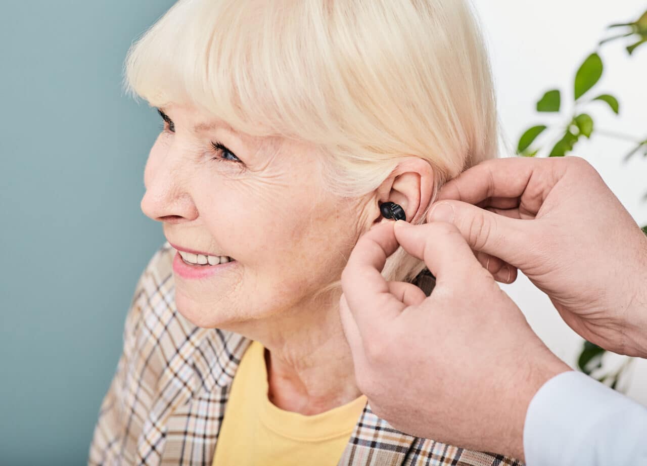 Happy senior woman getting fitted with a hearing aid by her audiologist.