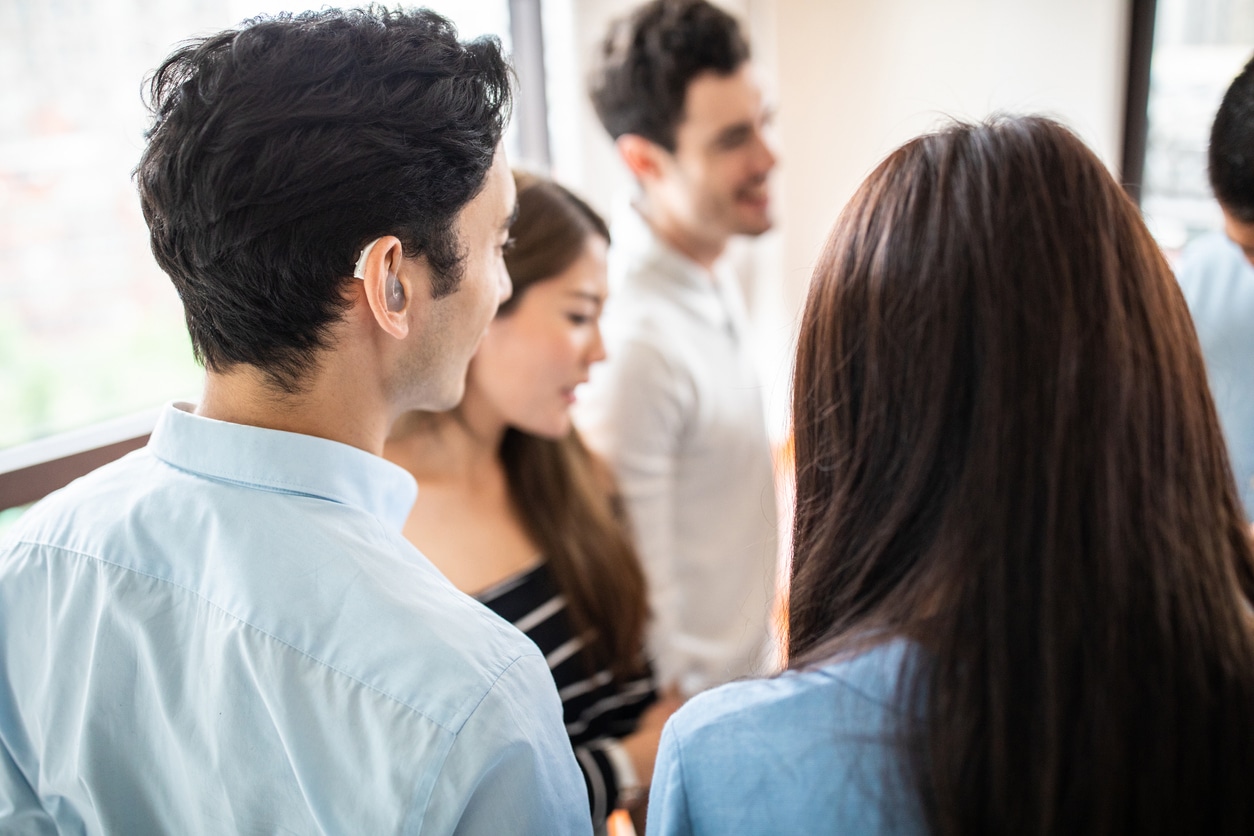 Young man with a hearing aid chatting with a group of people.