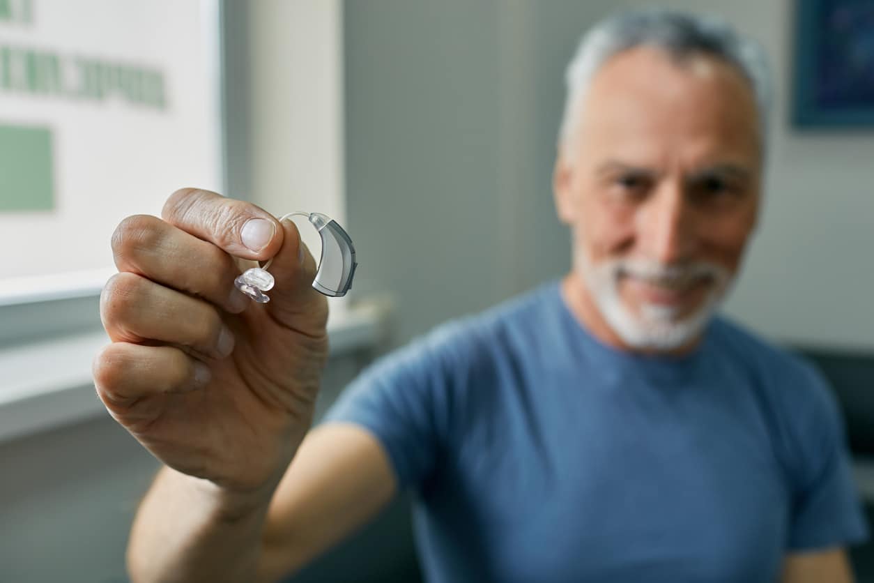 Senior man holding up new hearing aid.