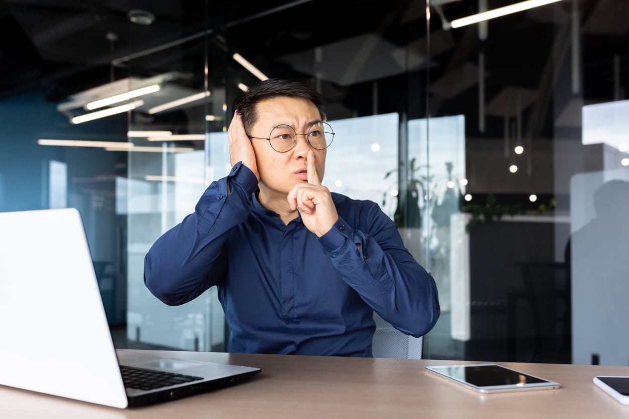 Person in office shushing a loud noise, covering his ear.